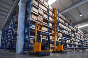 Two forklifts operating in a large warehouse with high-density pallet racking