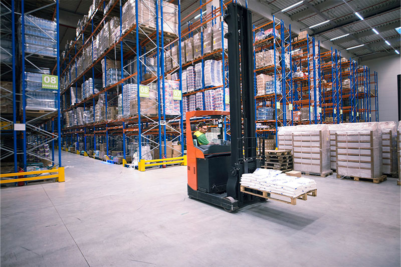 Warehouse worker operating a forklift to transport goods in a large storage facility with stacked shelves and organized inventory. forklift collision warning forklift safety