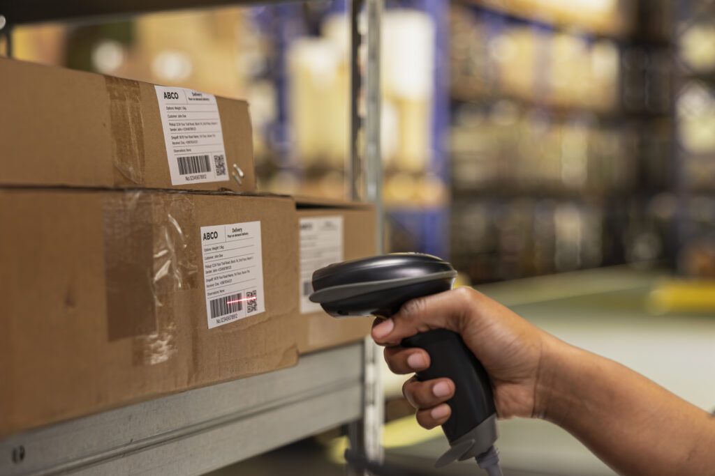 What Is RFID Asset Tracking? How It Works and Where It Fits 4 Warehouse worker scanning barcode labels on packages in a storehouse, illustrating manual asset tracking processes that RFID asset management systems replace