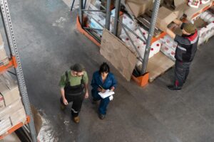 Warehouse workers conducting manual inventory tracking with clipboard and paper in an industrial storage facility representing asset management processes that RTLS replaces