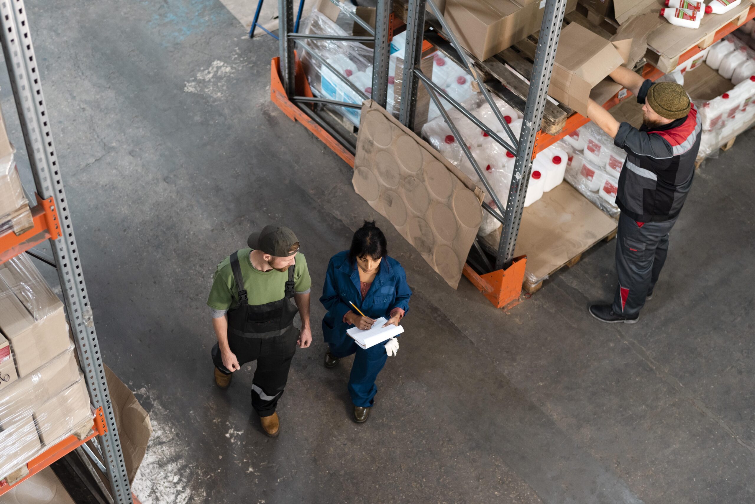 Home 67 Warehouse workers conducting manual inventory tracking with clipboard and paper in an industrial storage facility representing asset management processes that RTLS replaces