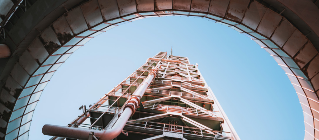 Overcoming Challenges During Turnaround: RTLS for a Fortune 10 Oil and Gas Company 2 Oil and gas refinery tower viewed from below through an industrial arch structure representing the complex facilities where Litum RTLS improves safety and efficiency