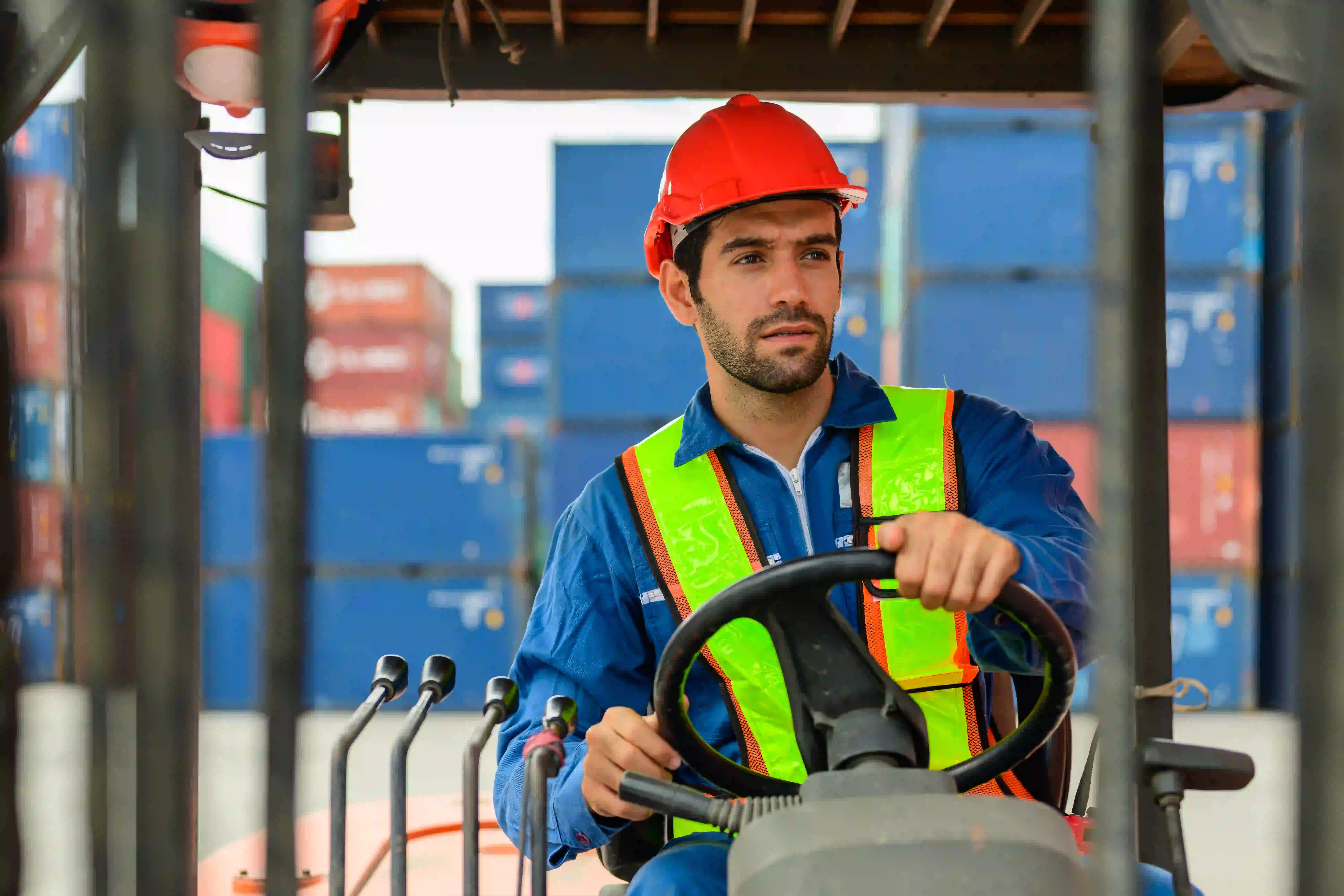 Home 79 Forklift operator in a hard hat driving through a busy distribution center aisle.