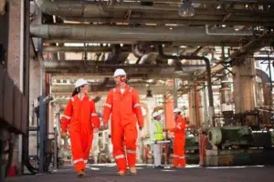Workers walking through an oil refinery wearing PPE, RTLS hazardous area personnel tracking supports safety compliance and emergency mustering in petrochemical facilities