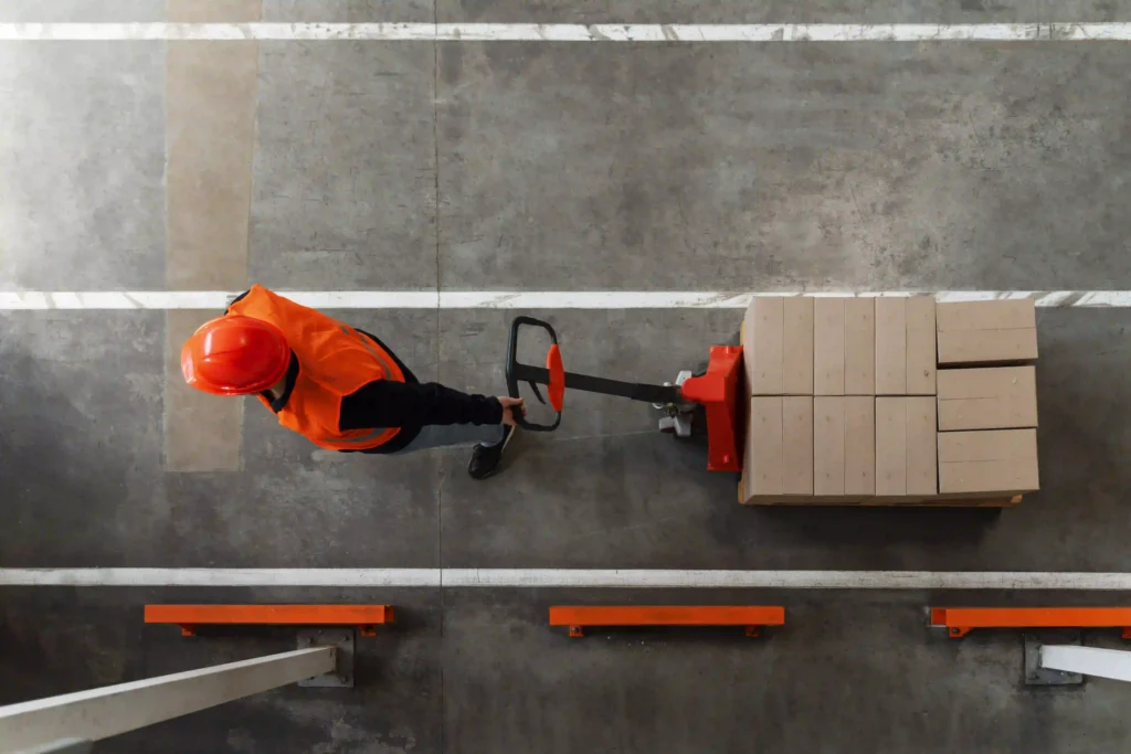 OSHA Forklift Certification in 2026: What the New Behavioral Monitoring Requirement Means for Your Operation 4 Overhead view of warehouse worker operating pallet jack near pedestrian walkway
