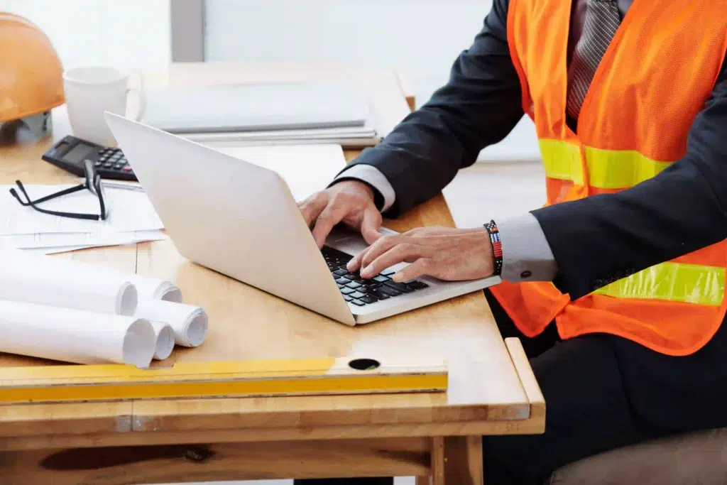 How Does Real-Time Location Tracking Improve Warehouse Safety? 2 Operations manager in a safety vest reviewing warehouse safety data and incident reports on a laptop at a desk