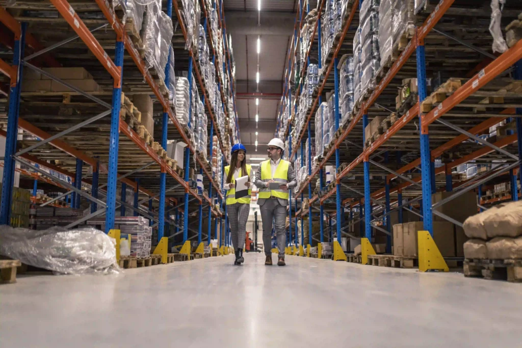UWB vs BLE for Industrial Tracking: A Practical Decision Guide 1 Workers with hardhats and safety vests walking through a warehouse aisle alongside forklift operations