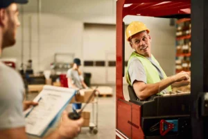 Warehouse worker reviewing a paper checklist beside a forklift operator, illustrating manual safety processes