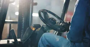 Close-up of a forklift operator's hands on the wheel inside the cab